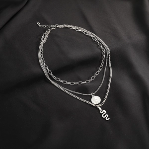 Close-up of layered silver chain necklace with snake and coin pendants on black silk