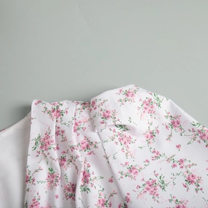 Dettaglio di un abito estivo bianco a fiori rosa con raffinate trame a pieghe sottili