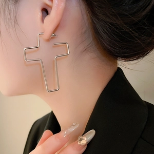 Gros plan d'un mannequin portant de grandes boucles d'oreilles croix en métal argenté