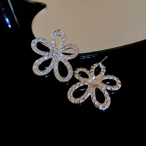Macro shot of silver flower earrings with crystals on a black reflective surface