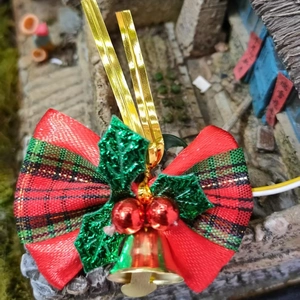 Detail of a red and green plaid Christmas bow with red berry bells and holly leaves