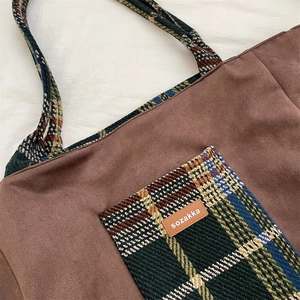 Détail du sac cabas en suédine avec poche à carreaux et étiquette sur tissu texturé