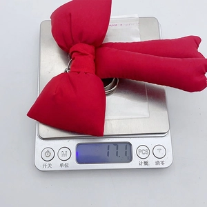 Detail shot showing the lightweight 17.1g red fabric bow keychain on a scale