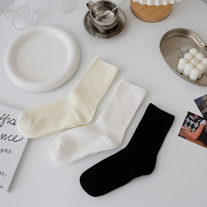 Three pairs of ribbed knit crew socks in beige, white and black colors for daily wear