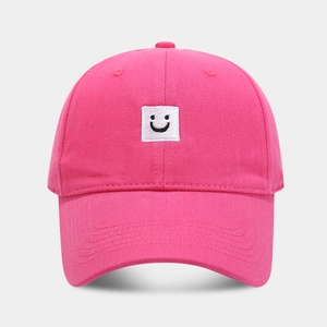 Détail d'une casquette rose en coton avec écusson carré brodé d'un visage souriant