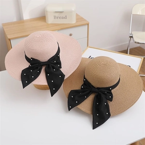 Detail view of wide brim straw hats with black satin ribbons and faux pearl bows