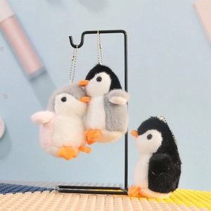 Detailed close-up of three plush penguin keychains in grey and black displayed on a stand