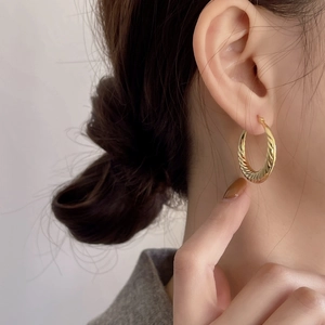 Close-up of golden twist hoop earring with wave texture on a female model's ear