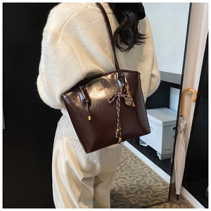 Détail du sac cabas brillant marron foncé avec nœud décoratif et finitions dorées