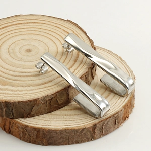 Detailed view of silver twisted bar earrings on natural wood blocks against white background