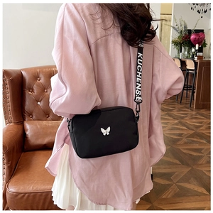 Detail view of the black nylon crossbody bag with butterfly decor and wide lettered strap