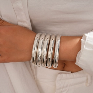 Close-up of five-piece polished silver metal geometric round bangles on a model's wrist