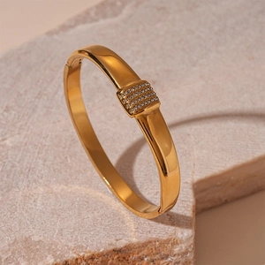 Detail of gold geometric bangle featuring four rows of crystals on a stone display