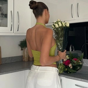 Détail du top en maille dos nu vert avec pantalon blanc dans un décor intérieur moderne