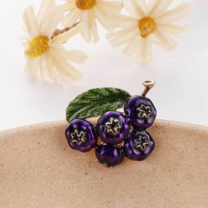 Elegant purple enamel blueberry brooch with green leaf detail on a ceramic surface