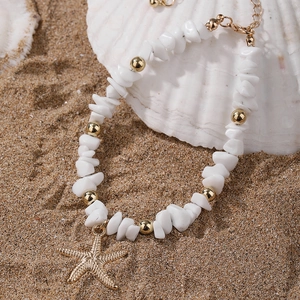 Detail of beaded anklet with white stones, gold beads and a starfish charm on beach sand