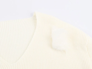 Nahaufnahme von cremefarbenem Strickpullover mit V-Ausschnitt und weißen Pelz-Applikationen
