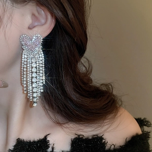 Close-up of heart-shaped tassel earrings with sparkling rhinestones on model's ear