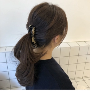 Detail of a leopard print banana hair clip worn by a model against a white tile wall