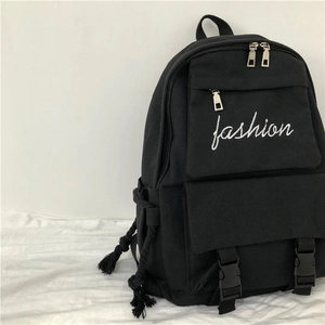 Detail of black canvas backpack showing front buckled pockets and fashion embroidery