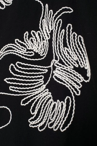 Close-up of intricate white embroidery on high-quality black fabric of the loose shirt