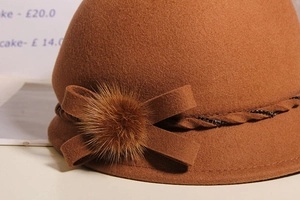 Detailed view of brown wool cloche hat featuring a plush fur ball and bow embellishment