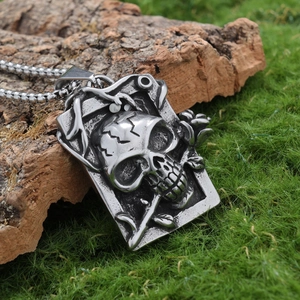 Gothic stainless steel skull and rose relief pendant on ball chain over mossy background