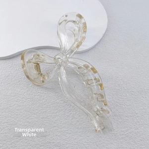 Detail of a transparent white bow-shaped hair claw clip with golden accents and metal spring