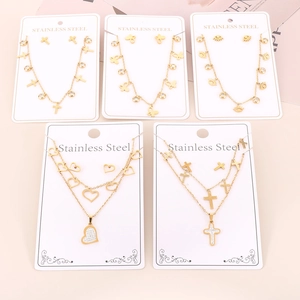 Golden stainless steel jewelry sets with cross, butterfly and heart pendants on pink backdrop