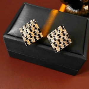 Gros plan détaillé de boucles d'oreilles carrées en or avec damier de zircons noirs et blancs