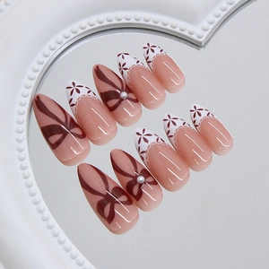 Faux ongles fleurs à la française avec nœuds rouges et perles sur un plateau