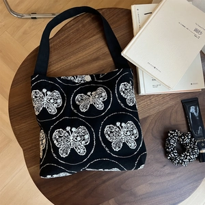 Detailed embroidery of white butterfly on black canvas bag with wide shoulder strap