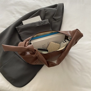 Minimalist brown faux leather croissant bag with pleated details on a gray blazer
