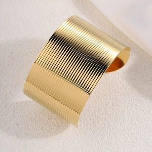 Detail of a wide gold cuff bracelet featuring elegant vertical ribbed patterns and textures