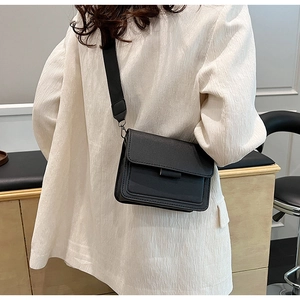 Detail of a black PU leather crossbody bag with wide strap on a model wearing white