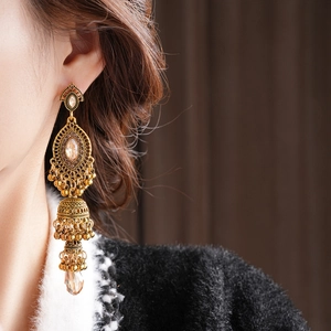 Gros plan de boucles d'oreilles Jhumka à trois niveaux dorées et cristaux champagne