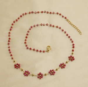 Close-up of gold stainless steel necklace featuring red faceted crystal flower charms