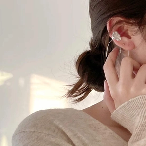 Close-up of minimalist silver flower ear cuff with delicate curved metal pendant on model