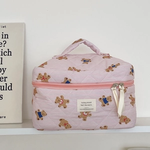 Detail of pink striped bear cosmetic bag with quilted texture and zipper on white shelf