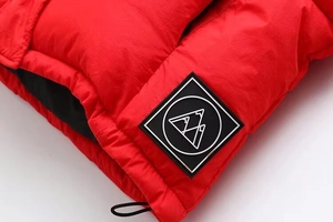 Détail macro de doudoune rouge montrant le tissu imperméable et le logo montagne noir