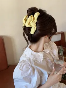 Detail of yellow pleated fabric hair claw clip shown on long hair from a back view