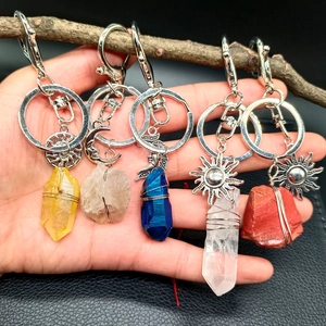 Five assorted natural crystal sun and moon keychains on a rustic branch with leather background