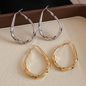 Close-up of minimalist twisted teardrop hoop earrings in gold and silver finishes
