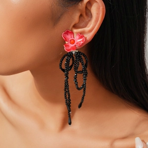 Detail of flower earrings with red petals and long black beaded tassels on model