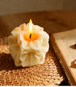 Primer plano de una vela perfumada con forma de peonía encendida en un tapete tejido