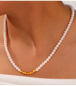 Detail of beaded pearl necklace with gold cube accents on a model neck