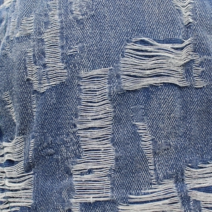 Primo piano del tessuto denim blu lavato con dettagli usurati e bordi sfilacciati