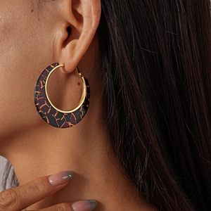 Macro shot of large golden hoop earrings with tortoiseshell resin texture on model