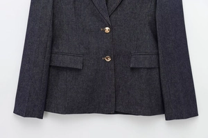 Close-up of deep blue denim blazer featuring gold metallic buttons and pocket details
