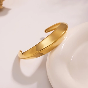 Detalle de un brazalete ancho de oro pulido con un diseño minimalista y aerodinámico